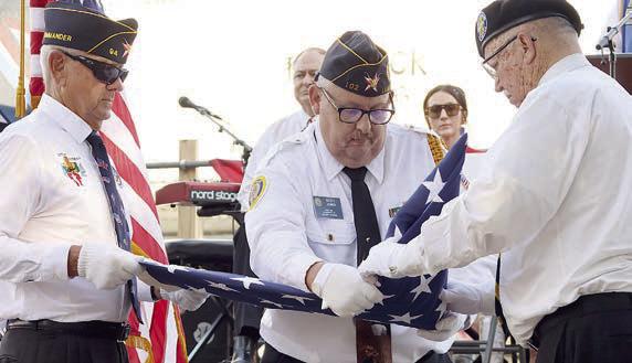 Flatonia American Legion Post 94 Commander Danny Vyvjala (left), La Grange Post 102 member Scott Jones (center), and Vietnam Veterans of America Chapter 870 President Andy Janda (right) fold the flag while Schulenburg Legion Post 143 Commander Bob Heinrich explains the meaning of the solemn act.