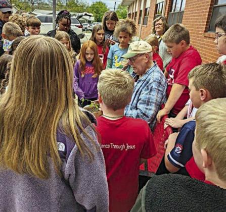 Master Gardener Wallace Brown demonstrates how to plant tomatoes surrounded by the students. Also shown is fourth grade teacher Jane Schneider.