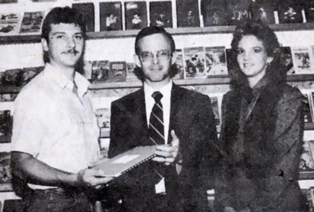 In 1988, Chamber of Commerce President Bill Dinger (center) welcomes The Record Rack as a member, presenting owners Bruce and JoAnn Lebeda with a membership packet. As noted in caption for the photo in the Sticker, the store at 527 North Main St. offered records, tapes, compact discs along with audio/video blank tapes and accessories while also renting VHS movies and machines, video cameras, and Nintendo action sets and games.