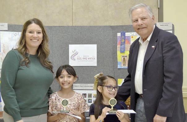POSTER CONTEST winners in Division 1 (grades K-2) were Reeanna Ramirez (second from left) and Daniela Albiter (second from right), both of Sacred Heart School in La Grange. Award sponsors were Cadence Bank, represnted by Megan Cooper (left), and Colorado Valley Communications, represented by Gene Kruppa (right).