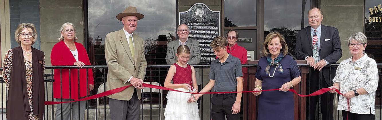 Conducting a ribbon cutting at the historical marker dedication this past Saturday are: (front, from left) Diana Mikesky, representing the Chamber of Commerce; Mark Elvig of Packard Law Center; Josephine and Jaxson Packard; Katrina Packard of Packard Law Center; Nina Howard, representing the Chamber of Commerce; (back, from left) Mayor Connie Koopmann; Gus and Karen Breymann; and County Judge Dan Mueller. Sticker Photo By Darrell Vyvjala