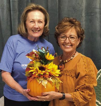 ABOVE – Helping to welcome fall with a blackout bingo prize she created is Martha Beckmann (right). Sharon Rodriguez (left) was the lucky winner.