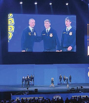 On the stage as seen on the “big screen” above it, Kaz McBride (center) and Grant Kubala (right) accept the National Chapter Award on behalf of the Schulenburg FFA at the National FFA Convention and Expo.