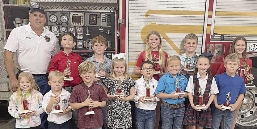 DIVISION WINNERS - Front, from left: Luke Hudec (1st place Kinder), Allie Neiser (2nd place Kinder), Paisley Guentert (3rd place Kinder), Ryker Demel (1st place Primary), Ree Lichnovsky (2nd place Primary), Tycen Mendel (3rd place Primary). Back, from left: Fire Chief Darren Guentert, JoLee Kuehn (1st place Intermediate), Brody Brossmann (2nd place Intermed.), Micah Garcia (3rd place Intermed.), and Brielle Goedrich (2nd place Middle). Not shown: Olivia Otto (1st place Middle), Noah Heger (3rd place Middle)