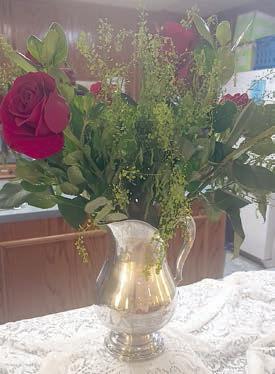 Centerpiece consisted of large red roses and greenery in a gold pitcher on a white lace tablecloth.