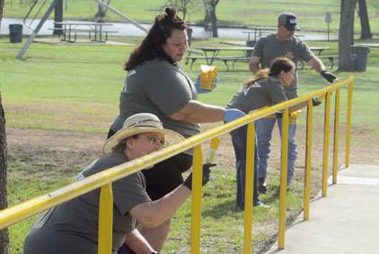 The railing to the entrance of the playground area at the Sports Complex gets a fresh coat of yellow paint thanks to four LCRA employees. Sticker Photo By Darrell Vyvjala