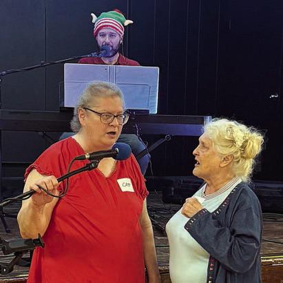 Helping to sing in German a Christmas carol played by Super Dave Hollas (back) are Cathy Besetzy (left) and Elena Pate (right).