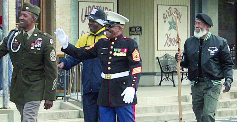 Representatives of the Army, Navy, Air Force, and Marines march through downtown as parade marshals, including Schulenburg natives Willie Matthews (waving) and Randy Houston (right). Sticker Photo By Darrell Vyvjala