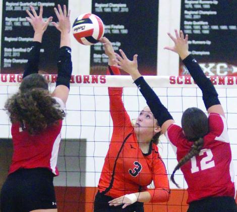 Reagan Dusek tips the ball away from two Lady Ricebird blockers for a point in the first set.