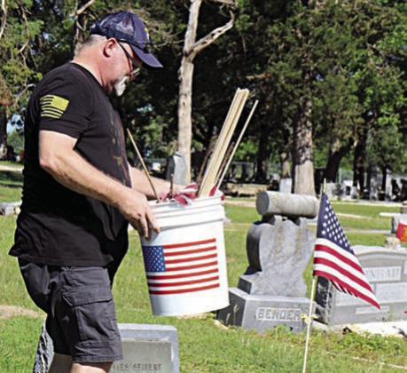 A flag on the grave of Floyd James Seifert in the Schulenburg City Cemetery is shown in the foreground at right, as Armen Herzik carries more flags to be placed on veterans’ graves. Seifert (Feb. 3, 1929-Sept. 22, 1960) served as a corporal in the infantry in the U.S. Army Reserves.