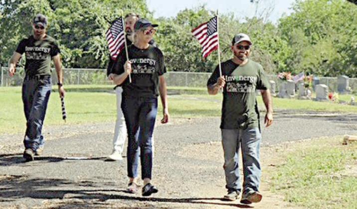 Volunteers fro m In venergy, which operates 7V Solar Ranch near Muldoon, walk along the road at the Schulenburg City Cemetery carrying flags to be placed on veterans’ graves. Invenergy not only provided volunteers to help with the project but also contributed financially toward the Schulenburg American Legion Post 143 flag fund.