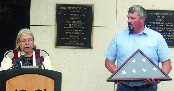 FLAG FROM SEN. CORNYN – Mayor Connie Koopmann reads a message  from U.S. Sen. John Cornyn and City Secretary Mason Florus displays the flag  flown over the U.S. Capitol that he sent for the occasion. Sticker Photo By Darrell Vyvjala