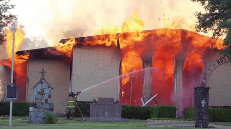 A firefighter from one of the four departments called to the Hostyn church fire attacks the raging flames at the front of the building. Sticker Photo By Darrell Vyvjala