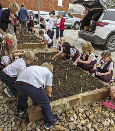 Planting their onion sets and planting lettuce and radish seeds from small cups are the St. Rose first graders. Kacy McBride, first grade teacher, stands at back left taking photos.