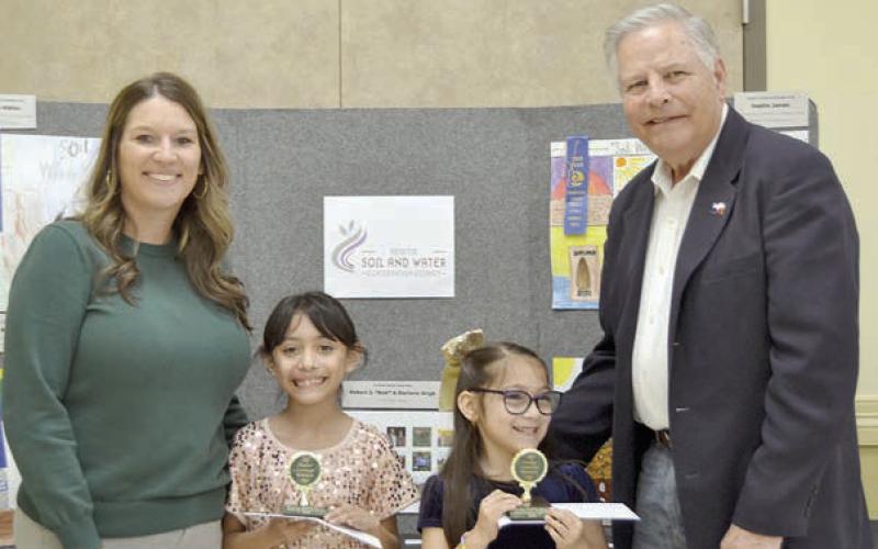POSTER CONTEST winners in Division 1 (grades K-2) were Reeanna Ramirez (second from left) and Daniela Albiter (second from right), both of Sacred Heart School in La Grange. Award sponsors were Cadence Bank, represnted by Megan Cooper (left), and Colorado Valley Communications, represented by Gene Kruppa (right).