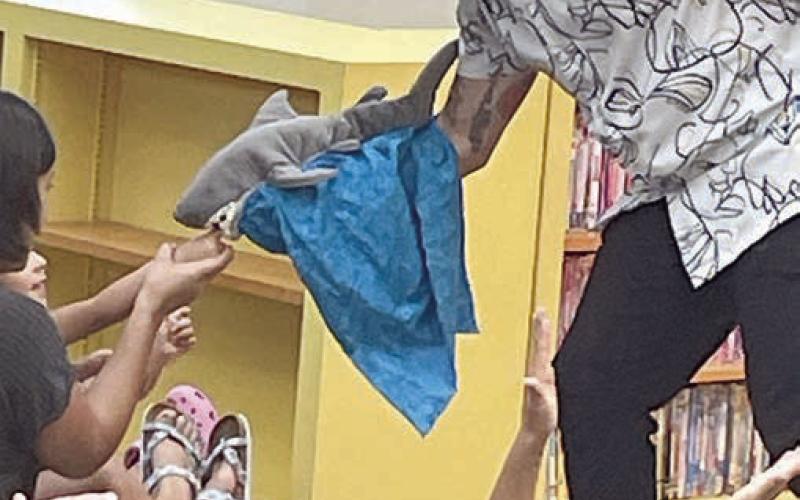 Mr. Leo’s shark puppet snacks on a youngster’s finger during last Friday’s show at the library. Sticker Photo By Darrell Vyvjala