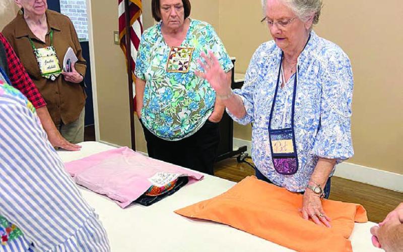 PHOTO ABOVE – Demonstrating label placement for pillowcases used to transport quilts is Pat Scherer, with Wilma Williams and Jackie Asbill observing.