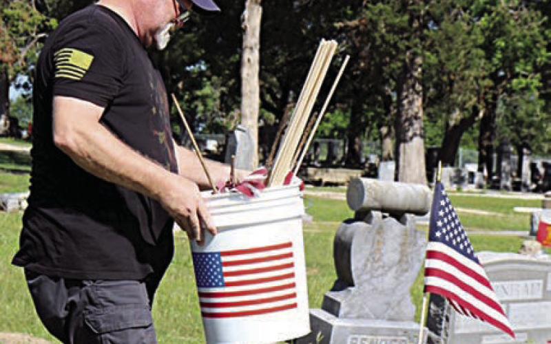 A flag on the grave of Floyd James Seifert in the Schulenburg City Cemetery is shown in the foreground at right, as Armen Herzik carries more flags to be placed on veterans’ graves. Seifert (Feb. 3, 1929-Sept. 22, 1960) served as a corporal in the infantry in the U.S. Army Reserves.