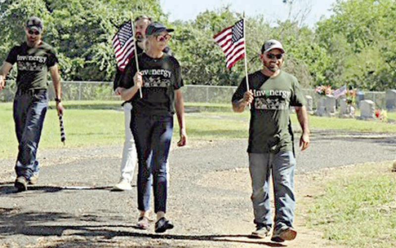 Volunteers fro m In venergy, which operates 7V Solar Ranch near Muldoon, walk along the road at the Schulenburg City Cemetery carrying flags to be placed on veterans’ graves. Invenergy not only provided volunteers to help with the project but also contributed financially toward the Schulenburg American Legion Post 143 flag fund.
