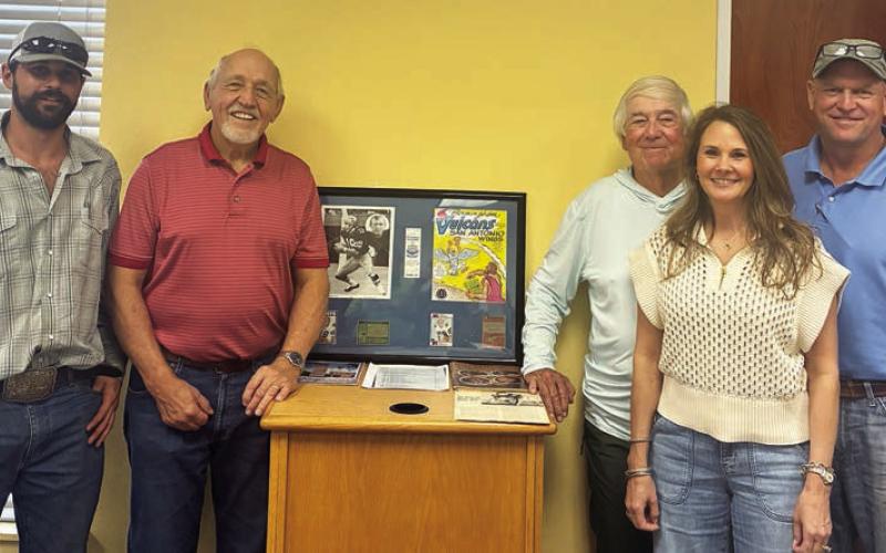 Standing with memorabilia from Hugo Hollas’ career at the book signing last Wednesday are authors Richard “Rico” Hollas (second from left) and Carl Duncan (third from right). Also shown is Hugo’s son, Shane (right) with his wife, Tonia, and his son, Jase (left). Sticker Photo By Dale Manning