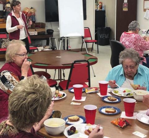 Guest Speaker – Paula Grahmann (standing at back left), owner of Your Hometown Pharmacy, was the lunch-and-learn speaker at NVCC on Monday, Nov. 29. Shown at the table in front finishing their meal while listening to Grahmann’s presentation are Judy Klesel (foreground left), Aileen Kasper (behind Klesel) and Irene Janda (right).