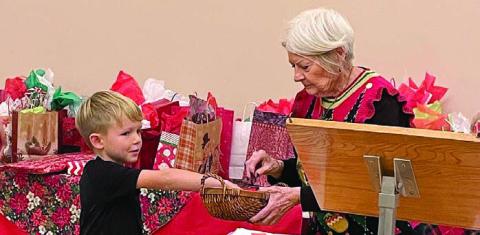 During the white elephant gift exchange, Dominik Woodworth (left) performs the drawing for who is next to choose a gift as Betty Danner holds the basket.