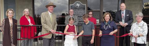 Conducting a ribbon cutting at the historical marker dedication this past Saturday are: (front, from left) Diana Mikesky, representing the Chamber of Commerce; Mark Elvig of Packard Law Center; Josephine and Jaxson Packard; Katrina Packard of Packard Law Center; Nina Howard, representing the Chamber of Commerce; (back, from left) Mayor Connie Koopmann; Gus and Karen Breymann; and County Judge Dan Mueller. Sticker Photo By Darrell Vyvjala