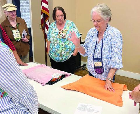 PHOTO ABOVE – Demonstrating label placement for pillowcases used to transport quilts is Pat Scherer, with Wilma Williams and Jackie Asbill observing.