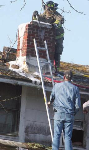 SVFD firefighter Travis Leihardt uses a foam and water mixture to contain Thursday’s chimney fire. Assisting is fellow SVFD member John Schindler. Sticker Photo By Darrell Vyvjala