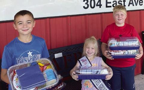 The Smrkovsky children – Gage, Abby and Wyatt – are shown delivering their donation of birthday party packages. Inside the cake pan is a cake mix, ready-to-eat icing, oil, plates, napkins, candles and balloons.