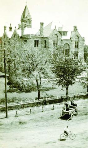 Circ a 1900 photo of the west side of the Courthouse taken from the second floor or roof of the Fink Building at 155 North Main in La Grange shows the iron fence that once surrounded the Courthouse. A wagon-drawn by a team of mules is tied to a hitching post, while a man is riding a bicycle down Main Street, which was still unpaved at the time. Photo Courtesy of Fayette Heritage Museum &amp; Archives