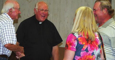 The Rev. Timothy Kosler (second from left) accepts a handshake and visits with a few of the parishioners at a farewell celebration. A steady stream of well-wishers came and went from the Knights of Columbus Hall for four hours last Wednesday. Sticker Photo By Darrell Vyvjala