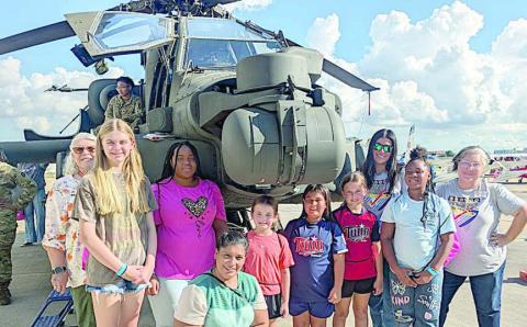 The Stanzel Museum group attending Girls in Aviation Day – shown in front of an Apache helicopter – included (from left) Ginger Friemel, grandparent; Vyvynne Friemel and Jade Williams, participants; Maria Camacho, parent; Emmalyn Pekar, Rebecca Camacho and Ella Pekar, participants; Melanie Ramirez, Stanzel Family Foundation program director; Ava Boston, participant; and Cynthia Fogleman, Stanzel Model Aircraft Museum director.