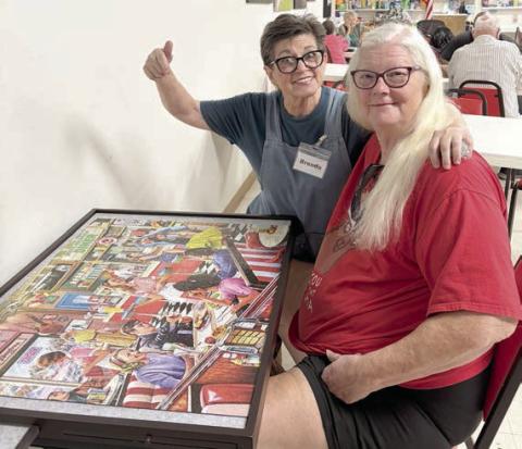 Showing off the puzzle that was completed after many hours of work by many people are (from left) volunteer Brenda Ray and member Kelly Ortiz.