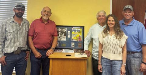 Standing with memorabilia from Hugo Hollas’ career at the book signing last Wednesday are authors Richard “Rico” Hollas (second from left) and Carl Duncan (third from right). Also shown is Hugo’s son, Shane (right) with his wife, Tonia, and his son, Jase (left). Sticker Photo By Dale Manning