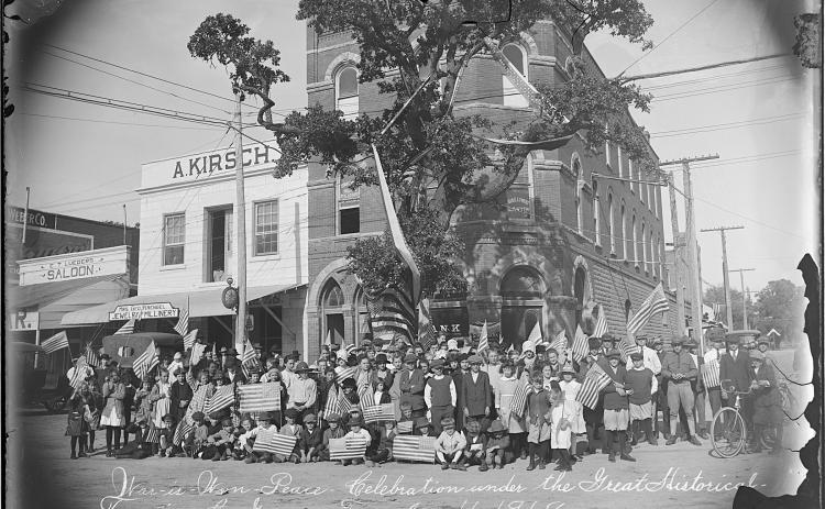 Louis Melcher’s photograph of a large group, including schoolchildren, holding American flags under La Grange’s Historic Oak, which is draped in patriotic bunting. The emulsion is pulling away from the edges of this glass negative on which was written: “War-is-Won-Peace-Celebration under the Great Historical Tree in La Grange, Tex. Nov. 11, 1918.”  Courtesy of Fayette Heritage Museum & Archives