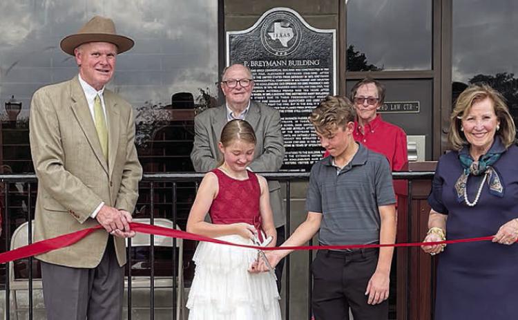 Conducting a ribbon cutting at the historical marker dedication this past Saturday are: (front, from left) Diana Mikesky, representing the Chamber of Commerce; Mark Elvig of Packard Law Center; Josephine and Jaxson Packard; Katrina Packard of Packard Law Center; Nina Howard, representing the Chamber of Commerce; (back, from left) Mayor Connie Koopmann; Gus and Karen Breymann; and County Judge Dan Mueller. Sticker Photo By Darrell Vyvjala