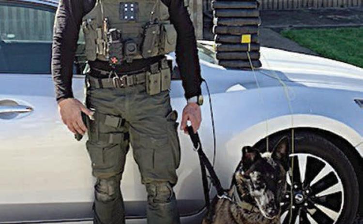 Sgt. Randy Thumann and Kolt pose in front of the Nissan Altima and the packages of cocaine they found after a traffic stop.