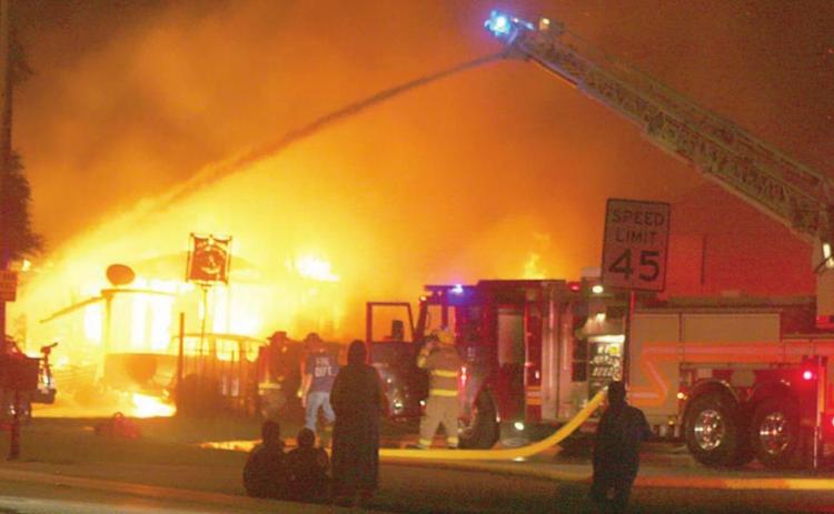 The SVFD’s ladder truck sends down a heavy stream of water to help get Tuesday morning’s structure fire under control while the Juarez family (center, in the foreground) watch helplessly as their house burns to the ground. Sticker Photo By Darrell Vyvjala