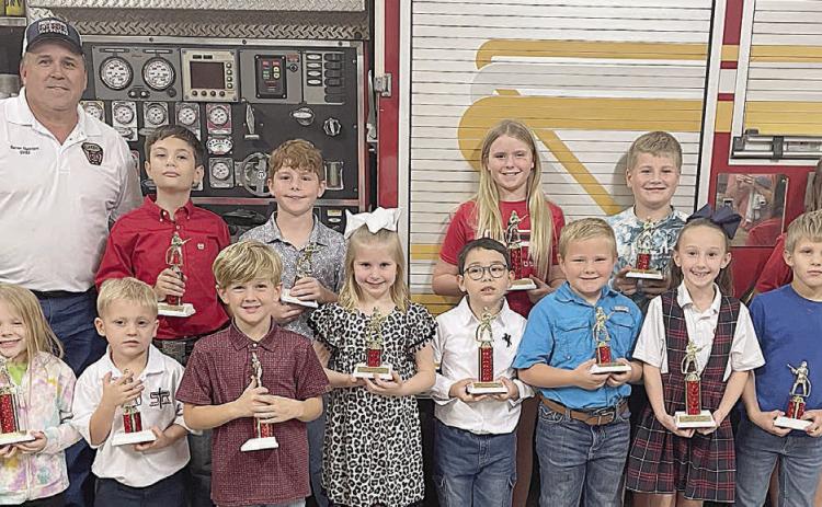 DIVISION WINNERS - Front, from left: Luke Hudec (1st place Kinder), Allie Neiser (2nd place Kinder), Paisley Guentert (3rd place Kinder), Ryker Demel (1st place Primary), Ree Lichnovsky (2nd place Primary), Tycen Mendel (3rd place Primary). Back, from left: Fire Chief Darren Guentert, JoLee Kuehn (1st place Intermediate), Brody Brossmann (2nd place Intermed.), Micah Garcia (3rd place Intermed.), and Brielle Goedrich (2nd place Middle). Not shown: Olivia Otto (1st place Middle), Noah Heger (3rd place Middle)