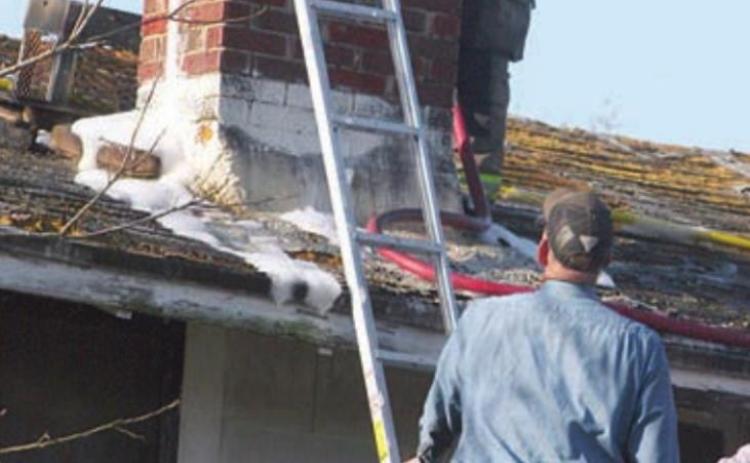 SVFD firefighter Travis Leihardt uses a foam and water mixture to contain Thursday’s chimney fire. Assisting is fellow SVFD member John Schindler. Sticker Photo By Darrell Vyvjala