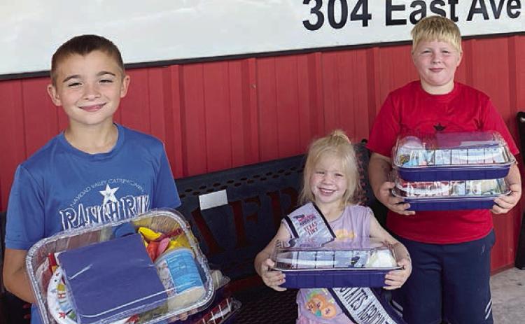 The Smrkovsky children – Gage, Abby and Wyatt – are shown delivering their donation of birthday party packages. Inside the cake pan is a cake mix, ready-to-eat icing, oil, plates, napkins, candles and balloons.