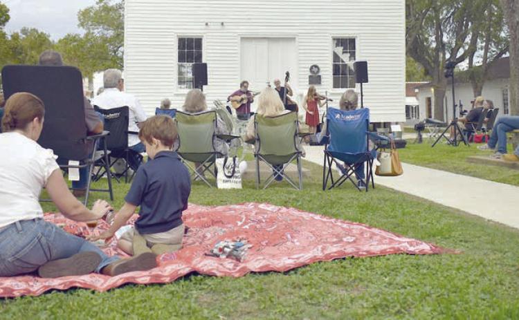 Arts for Rural Texas hosts a free live music series every March and October in Fayetteville on the historic courthouse lawn. Performers from a past series are shown in front of the courthouse while attendees with lawn chairs and picnic blankets enjoy the music.