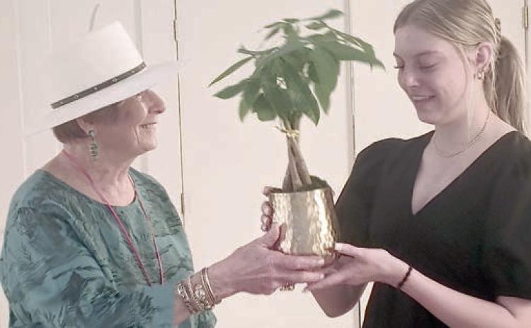 Scholarship recipient Kaylee Beyer (right) received a braided Money Tree plant from Nova Stonecipher (left).