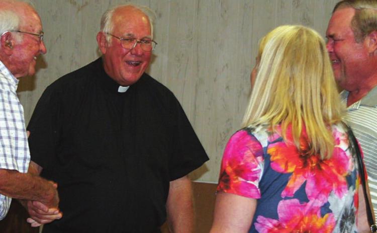 The Rev. Timothy Kosler (second from left) accepts a handshake and visits with a few of the parishioners at a farewell celebration. A steady stream of well-wishers came and went from the Knights of Columbus Hall for four hours last Wednesday. Sticker Photo By Darrell Vyvjala