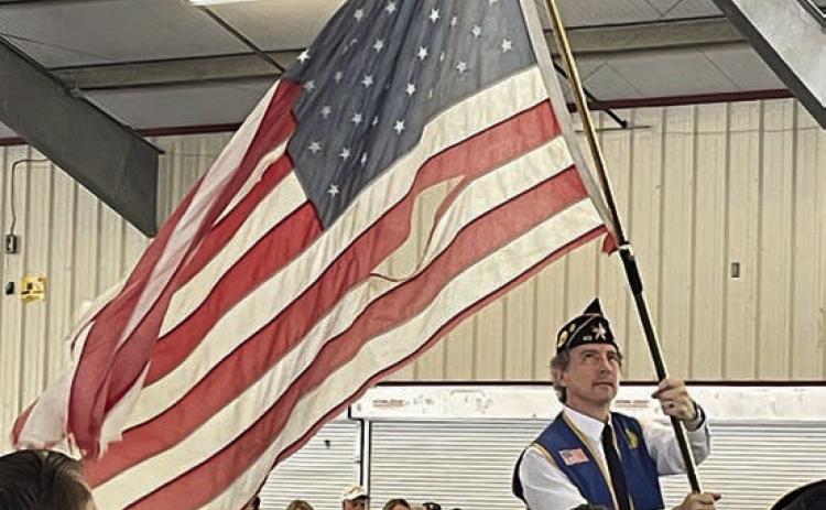 Post 143 First Vice Commander Ed Semler waves a tattered flag while the song “Ragged Old Flag” by Johnny Cash plays. Sticker Photo By Darrell Vyvjala