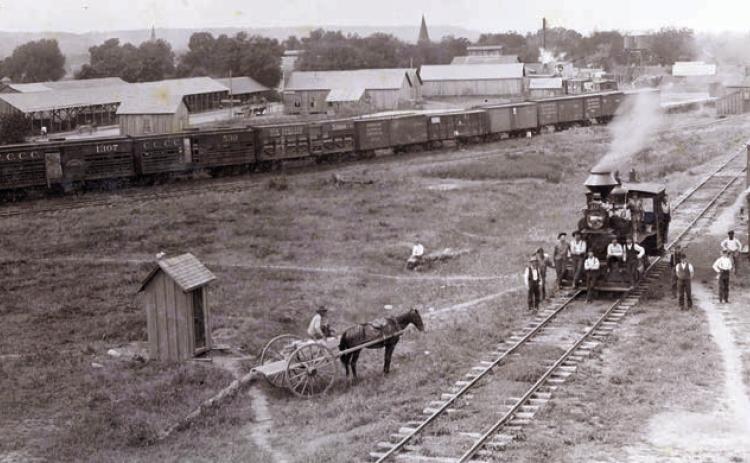 Circa 1895 photograph of the M.K.T. rail yard on the eastern end of La Grange (vicinity of 600th block East La Fayette Street) looking south with the bluff in the distance. Louis Melcher captured this view from the roof of the M.K.T. freight depot. Train cars, warehouses, elevated tanks and open sheds like those used by lumberyards are visible (present day Farmer’s Lumber Co.).