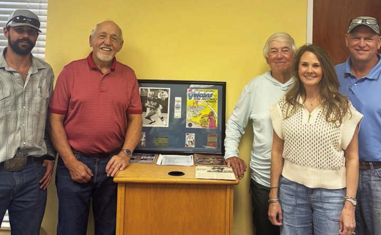 Standing with memorabilia from Hugo Hollas’ career at the book signing last Wednesday are authors Richard “Rico” Hollas (second from left) and Carl Duncan (third from right). Also shown is Hugo’s son, Shane (right) with his wife, Tonia, and his son, Jase (left). Sticker Photo By Dale Manning