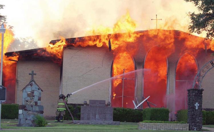 A firefighter from one of the four departments called to the Hostyn church fire attacks the raging flames at the front of the building. Sticker Photo By Darrell Vyvjala